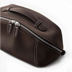 A dark brown makeup bag with silver zippers, white contrast stitching, and a top handle, shown on a clean white background. The brand name 'Leather Alliance' is subtly debossed on the front.