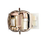 An open dark brown makeup bag with multiple compartments filled with cosmetics, shown from above on a white background. Visible items include a bottle, tubes, palettes, and a clear organizer panel with small accessories.