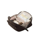 A dark brown zippered cosmetic bag shown open, revealing a light beige interior organizer with a clear plastic pouch and several makeup items inside, set against a plain white background.