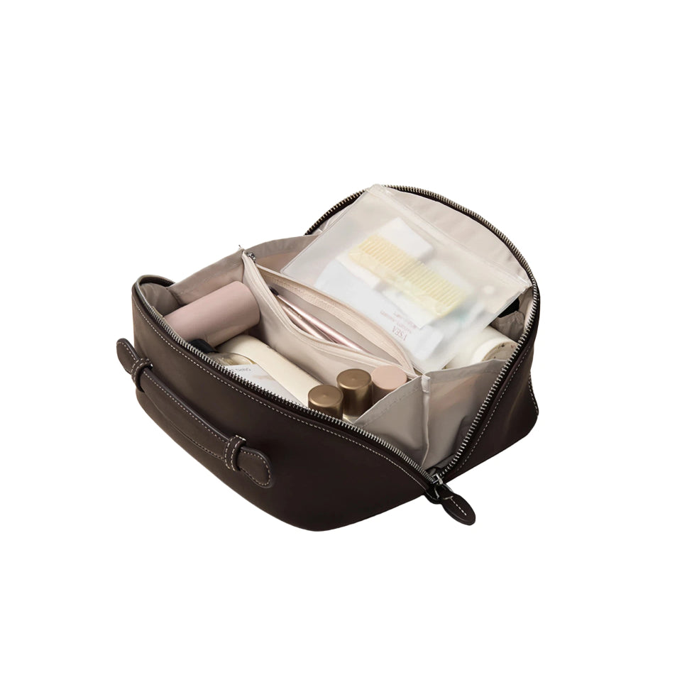 A dark brown zippered cosmetic bag shown open, revealing a light beige interior organizer with a clear plastic pouch and several makeup items inside, set against a plain white background.