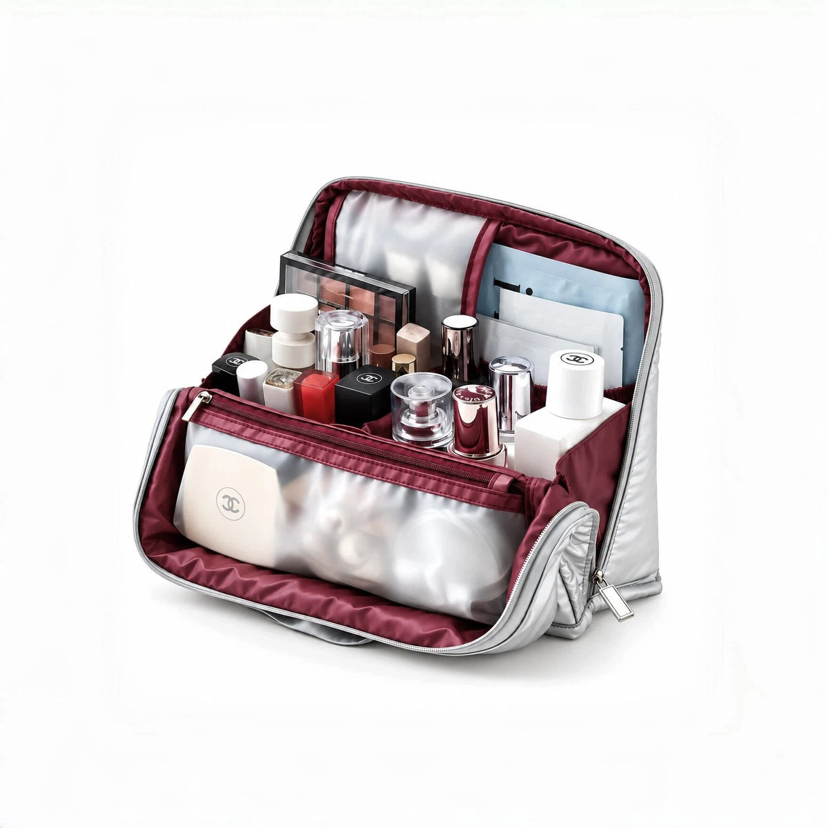 An open silver and burgundy cosmetic bag filled with makeup items, shown on a clean white background. A Chanel logo is visible on a cream makeup compact inside the bag.