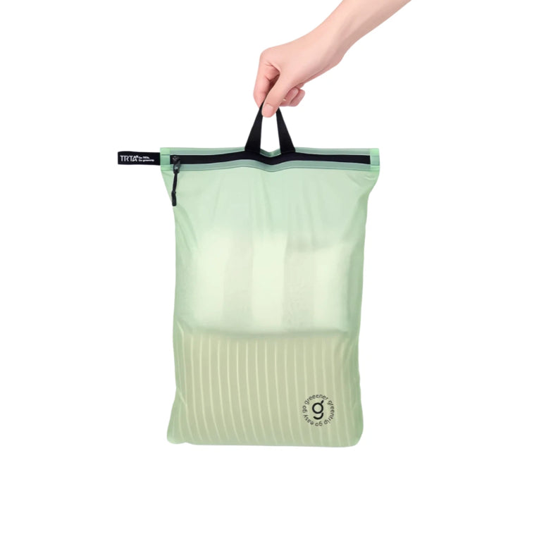 Light green travel bag with black zipper held by a hand on a white background