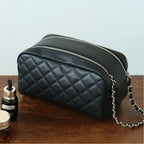 Black leather makeup bag with a chain detail on a wooden surface, next to a bottle and jar.