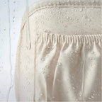 Close-up of a light beige or cream fabric surface with water droplets beaded on top and water droplets sliding off easily, demonstrating a waterproof or water-repellent finish.