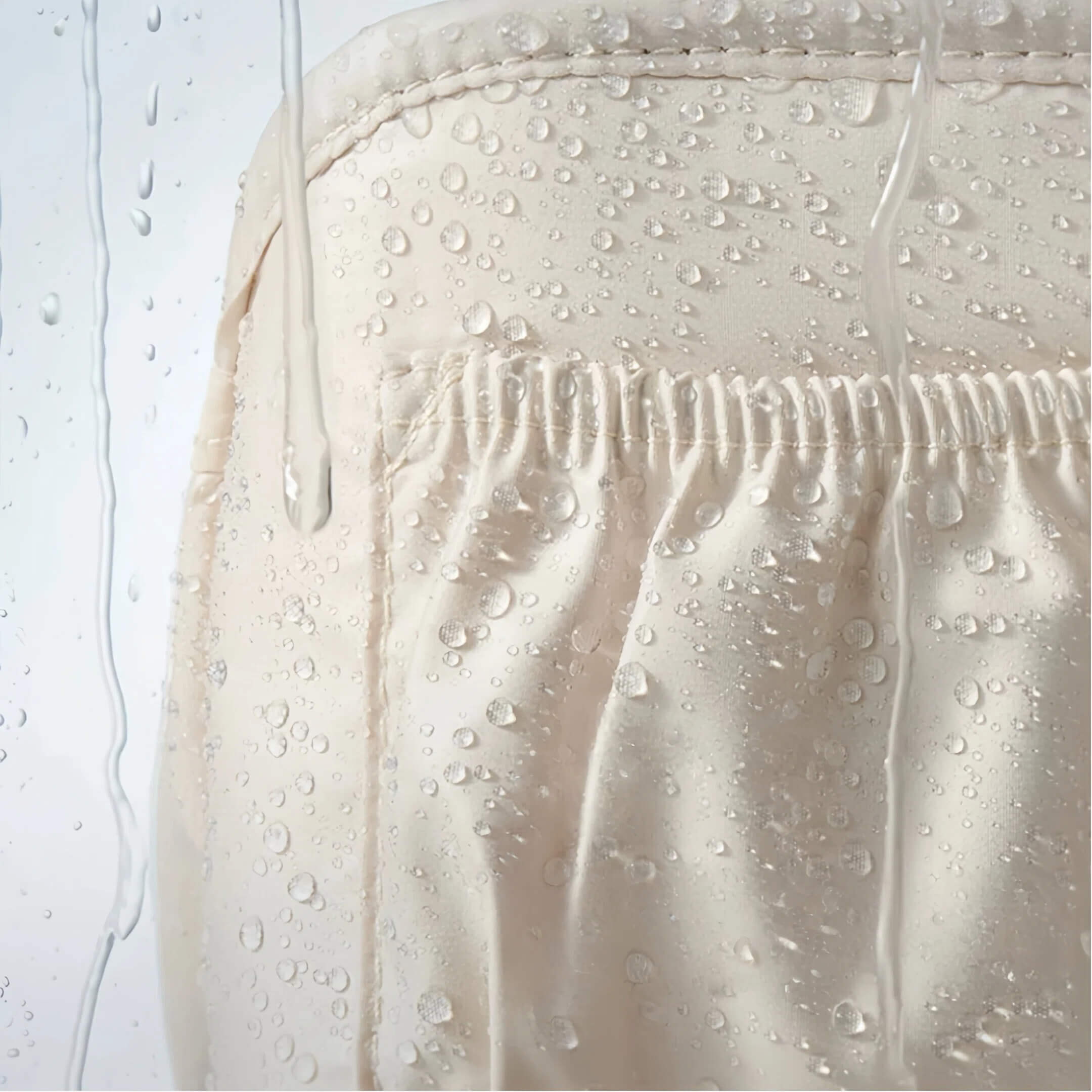 Close-up of a light beige or cream fabric surface with water droplets beaded on top and water droplets sliding off easily, demonstrating a waterproof or water-repellent finish.