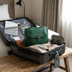 Green makeup bag inside an open suitcase with travel items on a wooden table.