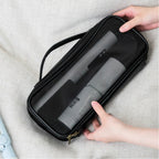 Black hairdryer case with a gray hair straightener inside, held by hands on a light gray fabric background.
