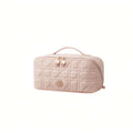 A light pink quilted cosmetic bag with a top handle, gold-tone zipper, and a small bear logo on the front, shown on a plain white background.