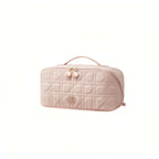 A light pink quilted cosmetic bag with a top handle, gold-tone zipper, and a small bear logo on the front, shown on a plain white background.