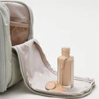 Foundation bottle with beige shade next to an open makeup bag on a light background