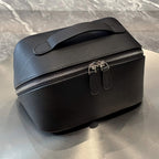 A black pebbled leather cosmetic bag with a top handle and dual zipper closures, resting on a reflective metallic surface.