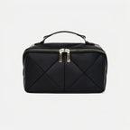 Black quilted makeup bag with gold zipper on a light gray background