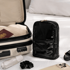 Black travel makeup bag next to an open suitcase with a passport and other items on a bed.
