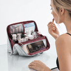 A woman applies lipstick while a silver and burgundy makeup bag sits open on a white table, filled with cosmetics and a phone inside.