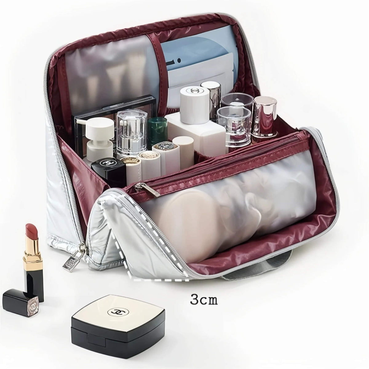 An open silver cosmetic bag with burgundy lining, shown filled with makeup items and a translucent pouch. A small lipstick and compact are placed beside it, with a '3cm' size marker on a clean white background.