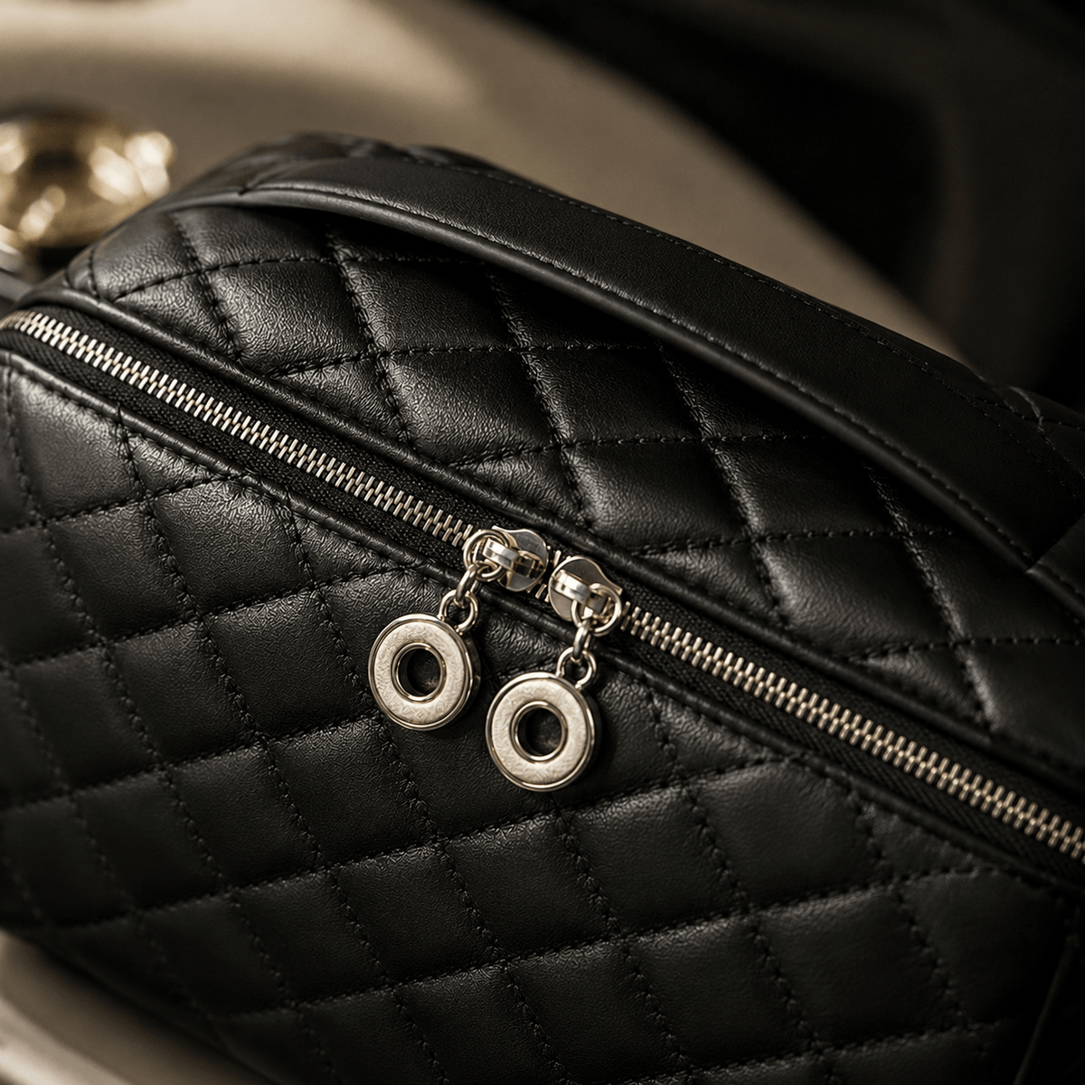 Close-up of a black quilted leather bag with silver-toned zippers and circular metal pull charms, photographed against a dark and softly blurred background.
