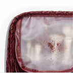 Close-up of a burgundy cosmetic bag showing a clear plastic window with visible brown powder residue or dust on the inside.