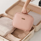 Person packing a pink toiletry bag into an open suitcase on a light background