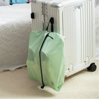 Green shoe bag with black zipper on a white suitcase against a neutral background
