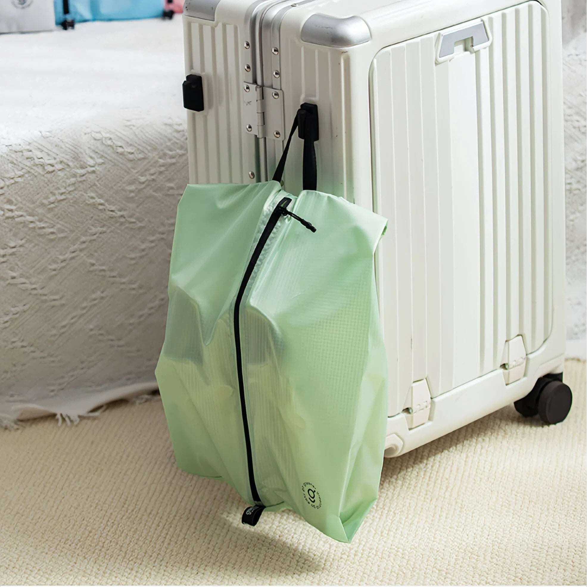 Green shoe bag with black zipper on a white suitcase against a neutral background