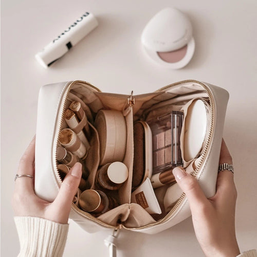 Open beige makeup bag with various cosmetic items on a light surface.