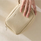 A hand holding a beige makeup bag