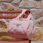 Pink bag with a character design hanging on a chair against a stone wall.