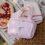 Pink travel bag with cartoon character on a wooden table with fruit and a blanket.