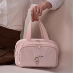 Pink travel bag with cartoon character design held by a person wearing a white shirt.