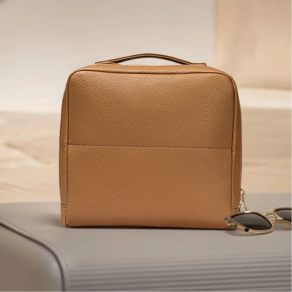 Brown makeup bag on a light surface with sunglasses on top