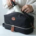 Person placing a bottle into a black toiletry bag with leather accents.