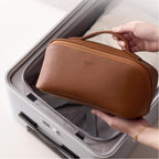 Brown travel case held by a hand in front of an open suitcase