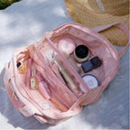 Open pink makeup bag with various cosmetic items on a light surface