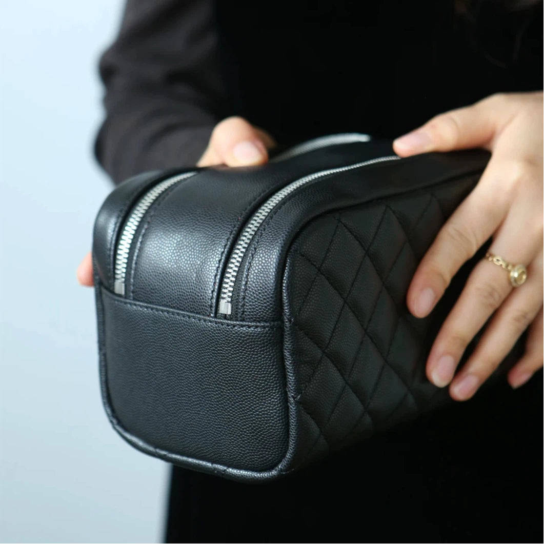 Person holding a black leather makeup bag with a zipper.