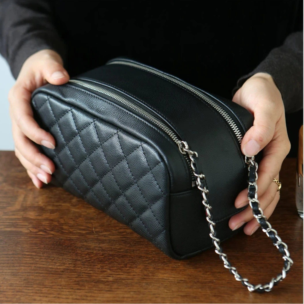 Black leather makeup bag with a chain strap held by a person on a wooden surface