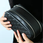 Black leather makeup bag with zippers held by a person against a light background