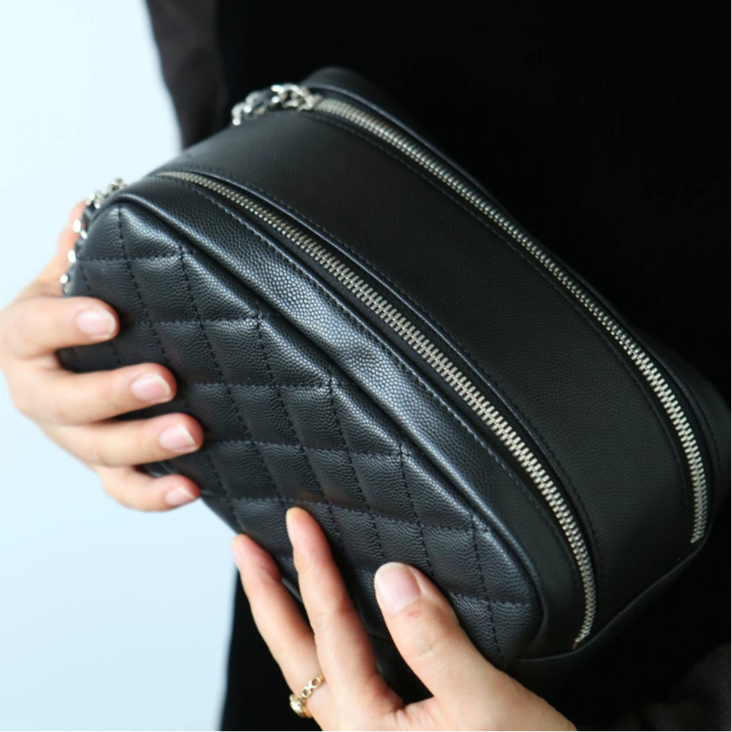 Black leather makeup bag with zippers held by a person against a light background