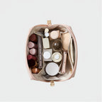 An open pink makeup bag filled with assorted cosmetics and skincare items, photographed from above on a clean light gray background.