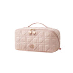 A light pink quilted cosmetic bag with a top handle, gold-tone zipper, and a small metallic logo on the front, shown on a plain white background.