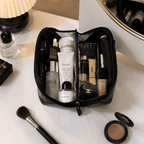 Open makeup bag with various skincare and cosmetic products on a marble surface.