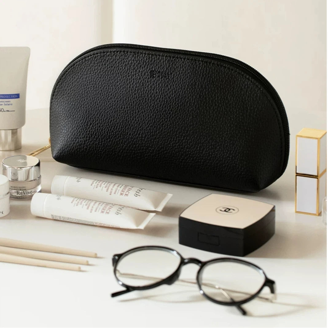 Black cosmetic bag on a white surface with skincare products and glasses.