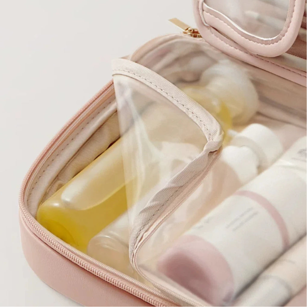 Pink toiletry bag with travel-sized products on a light gray background