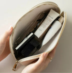 Hand holding an open beige makeup bag with skincare products on a neutral background
