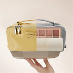 Makeup bag with a palette and tube of cream held by a hand on a beige background