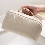 Beige toiletry bag with a handle being held over water, showing water resistance.