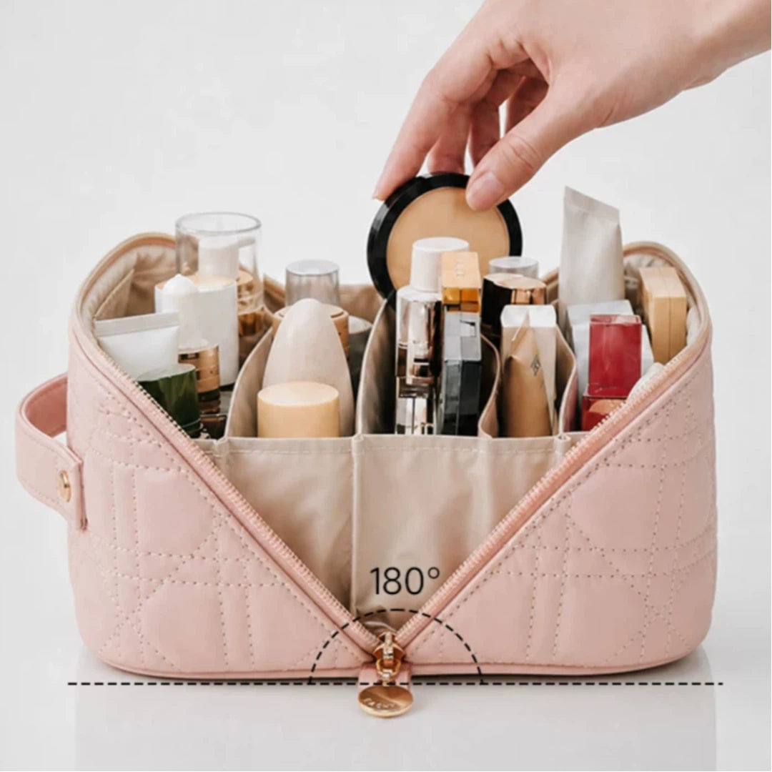 A light pink quilted cosmetic organizer bag filled with makeup items and skincare products, shown open with a hand placing a compact into one of the compartments. The front zipper area has a printed diagram indicating a 180-degree angle.