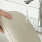 Beige cosmetic bag being tested for water resistant with a faucet in the background