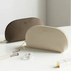 Two cosmetic bags, one brown and one beige, on a light surface with makeup items around.