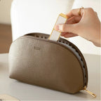 Hand placing a white and gold lipstick into a beige cosmetic bag.