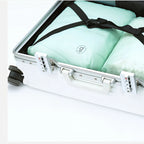 White suitcase with a green garment inside, secured with a black strap.